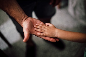 Mano de adulto extendida y encima mano de un niño representando la bondad y generosidad paternal